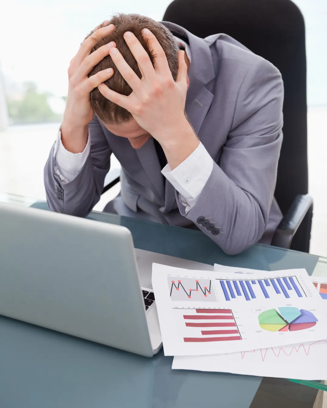 A businesswoman in an office looks frustrated while reviewing bills and finances with a laptop, displaying anxiety.