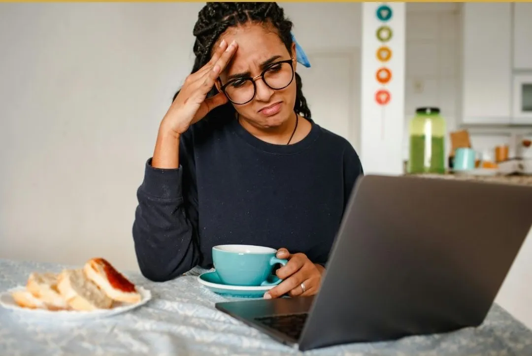 A businesswoman in an office looks frustrated while reviewing bills and finances with a laptop, displaying anxiety.